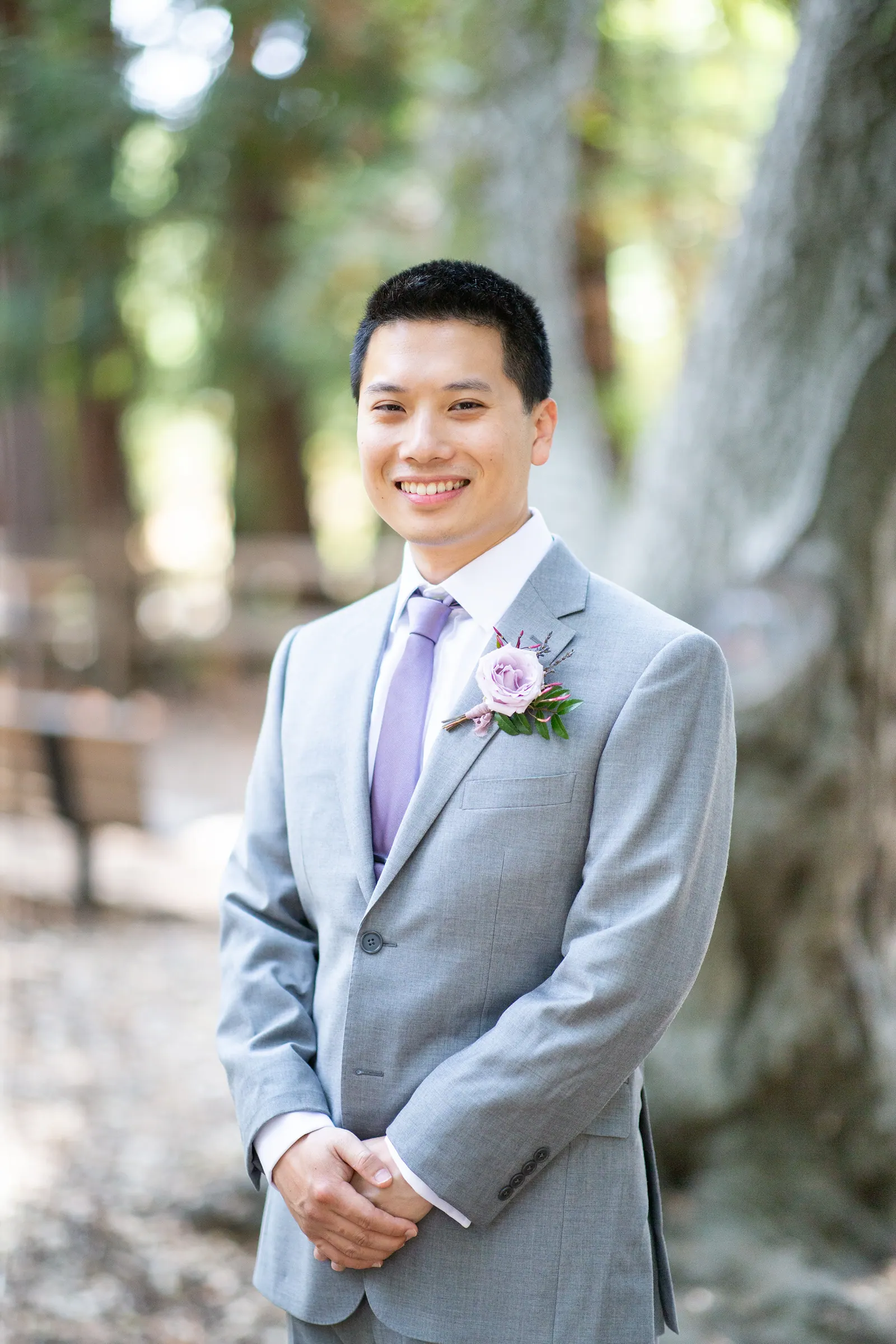 Groomsman in a grey suit smiling among redwoods