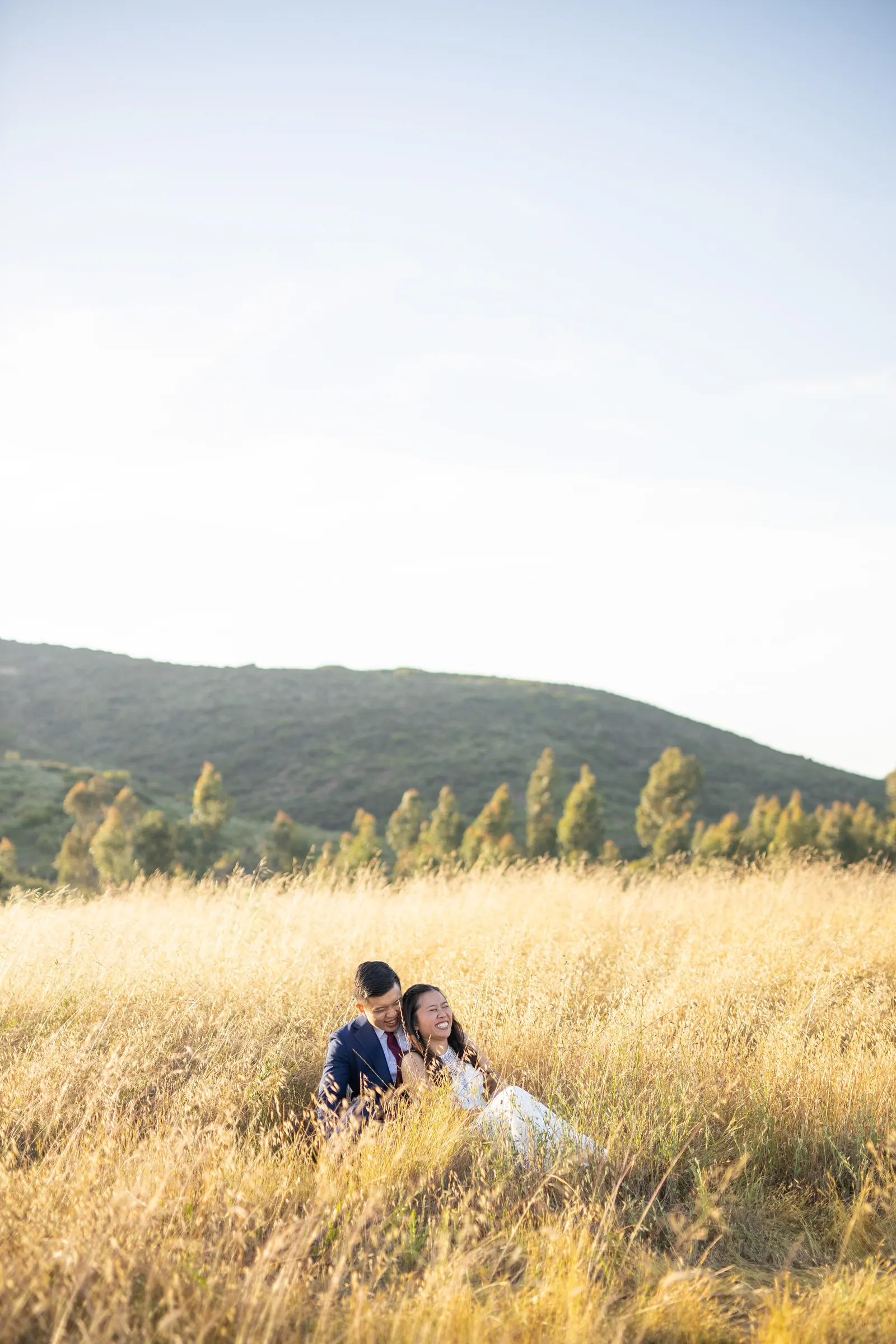 Couple lying in golden grass on a hillside at sunset