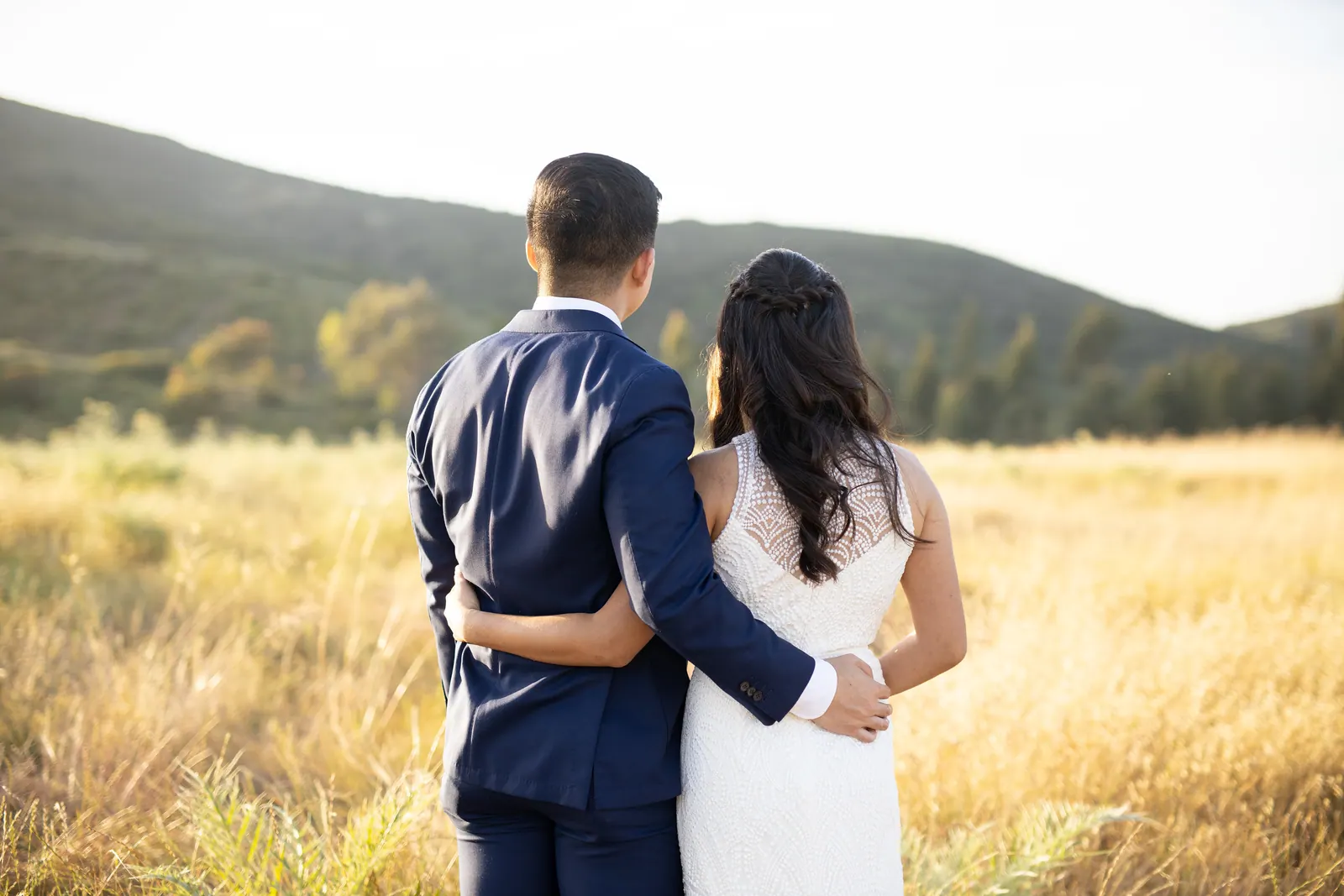 Bride and groom seen from behind looking over golden hills